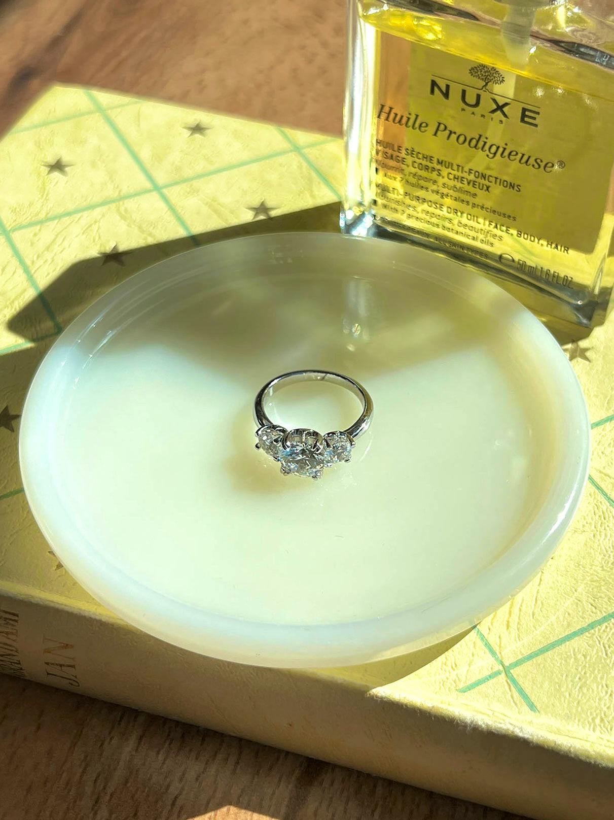 A Three Glow Ring placed on a white dish with a perfume bottle and box visible behind it.