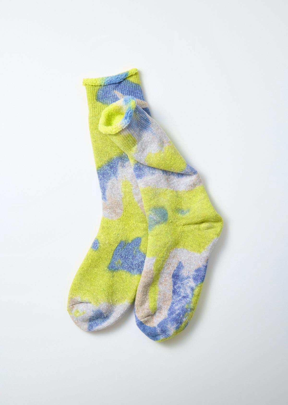 Pair of tie-dye pile socks in yellow, blue, and pale gray shown flat on a white background.