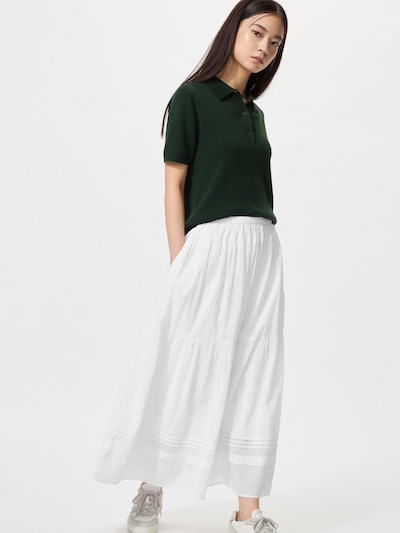 A model wearing the white tiered maxi skirt (shorter length) paired with a green polo top and sneakers.