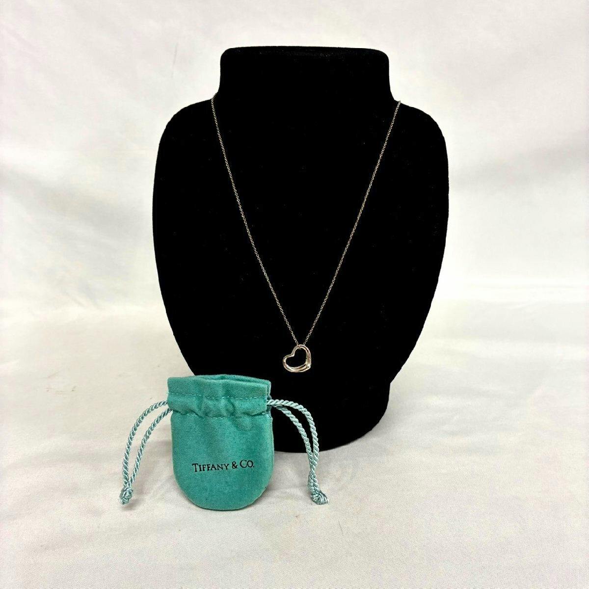 Tiffany & Co. open-heart necklace pendant displayed on a black necklace bust with a Tiffany pouch in front.