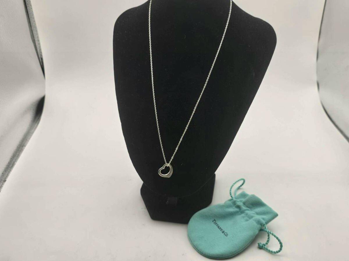 Silver open-heart pendant on a chain displayed on a black necklace bust with a small Tiffany pouch beside it.