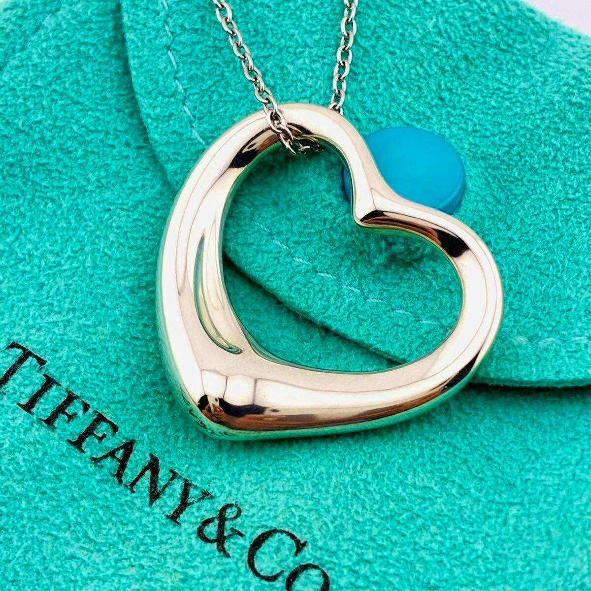Open-heart silver pendant necklace resting on a Tiffany blue pouch with part of the TIFFANY & CO. logo visible.