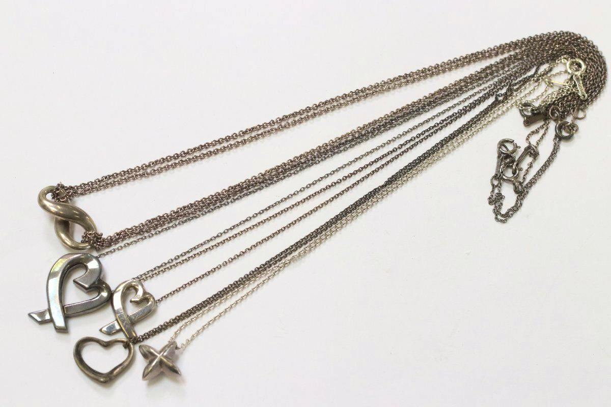 Five Tiffany & Co. silver necklaces with various pendants, including an infinity and open-heart, laid flat on a white background.