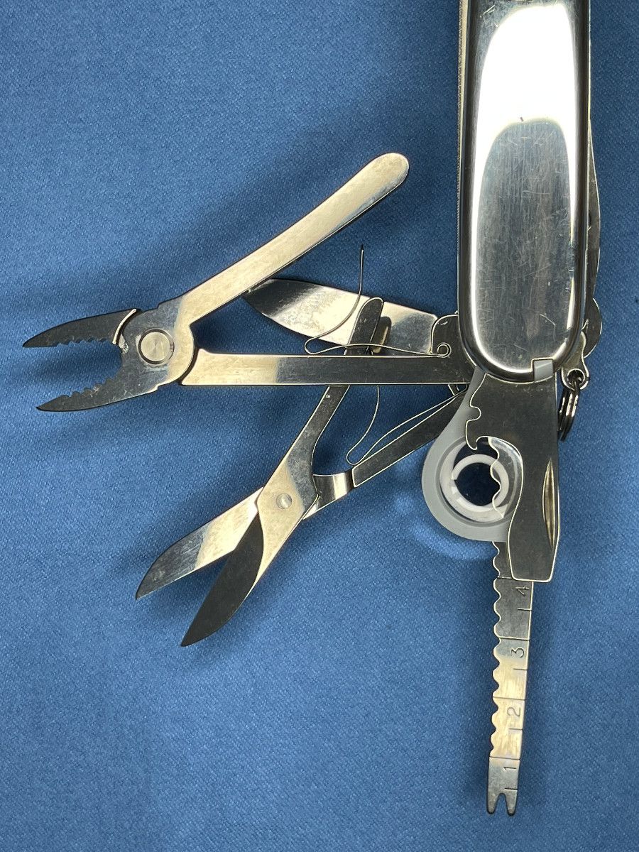 Silver Tiffany & Co. Victorinox multi-tool pocket knife with several tools extended (pliers, scissors, small ruler) on a blue background.