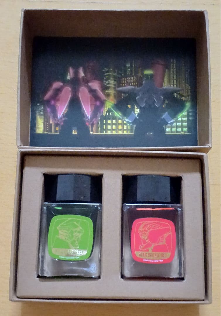 Two fountain pen ink bottles with green and red labels sitting in a cardboard gift box with character artwork inside the lid.