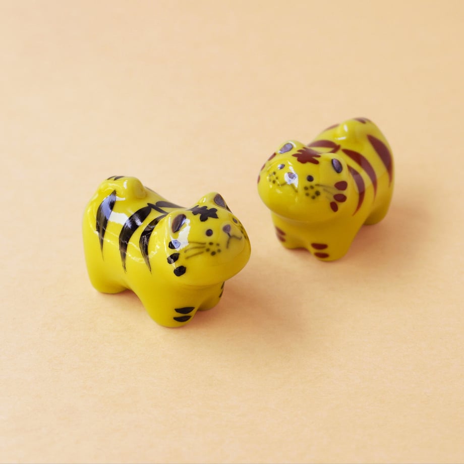 Two yellow ceramic tiger-shaped chopstick rests placed on a peach background.