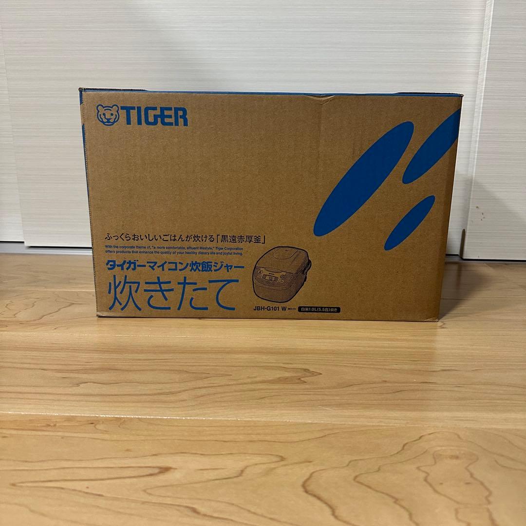 Cardboard box with TIGER logo and text indicating a rice cooker, sitting on a wooden floor.