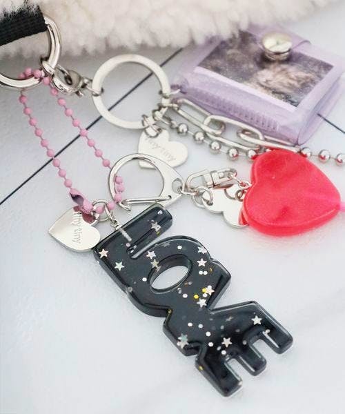 Black acrylic "LOVE" keychain charm with star glitter and attached red heart charm on a light surface.