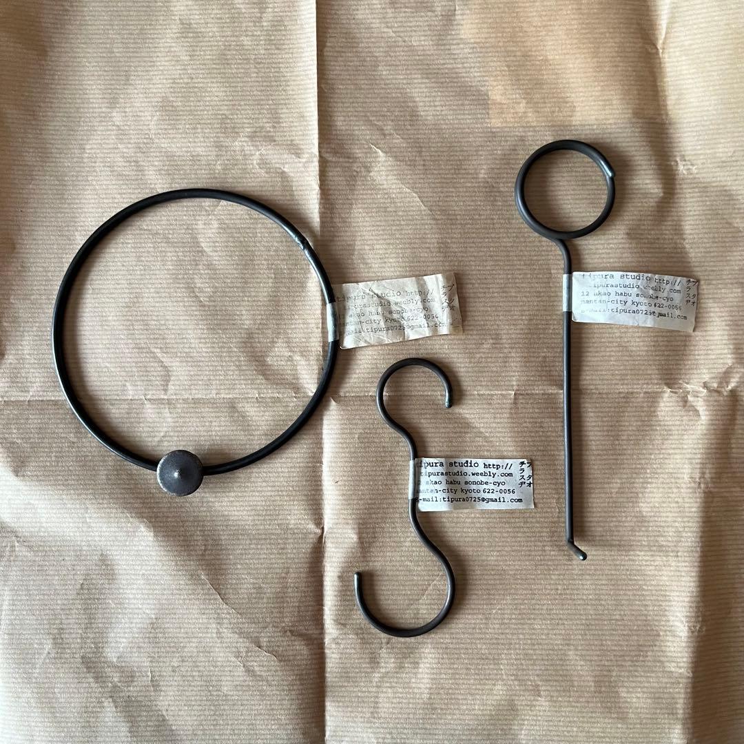 A circular iron ring and two S-shaped and L-shaped iron hooks laid on brown paper with small paper tags.