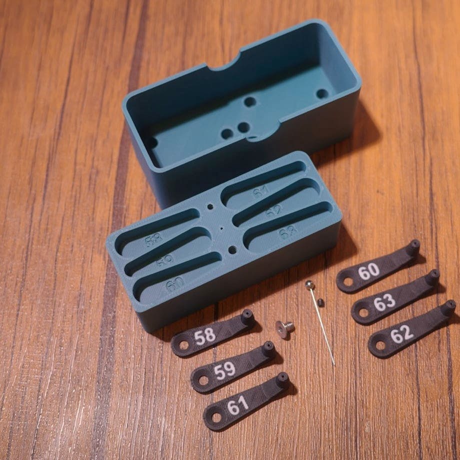 Opened plastic guide box with numbered plastic side guide parts and small metal pin and screw on a wooden surface.