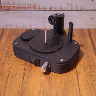 Black plastic tire glue helper tool with a circular toothed plate and two vertical posts on a wooden surface.