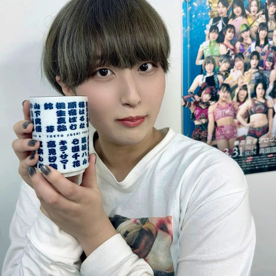 A person holding a white yunomi (Japanese teacup) printed with blue Japanese characters.