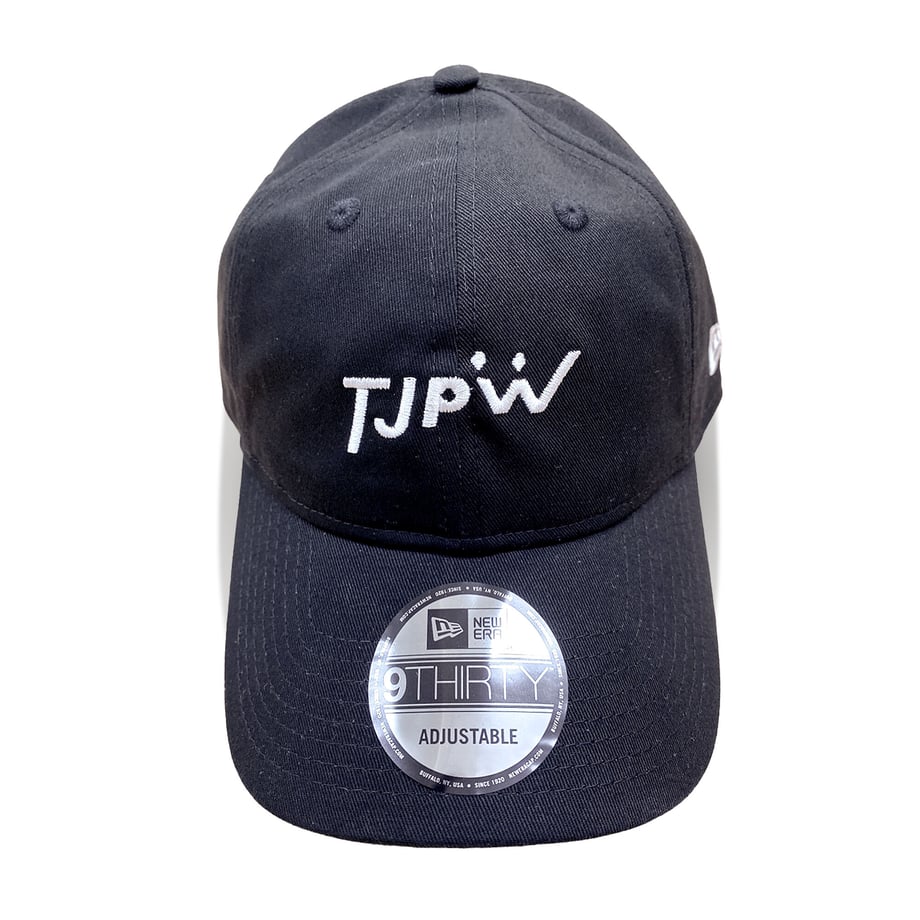 Front view of a black TJPW × NEW ERA 9THIRTY adjustable cotton baseball cap on a white background, showing the embroidered logo and brim sticker.