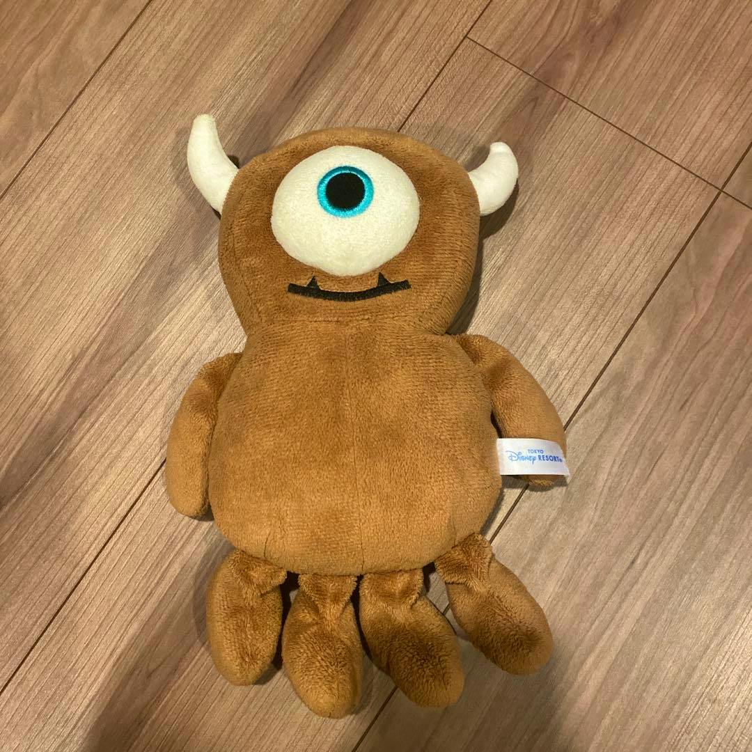 A brown Tokyo Disney Resort "Little Mikey" plush toy lying on a wooden floor.