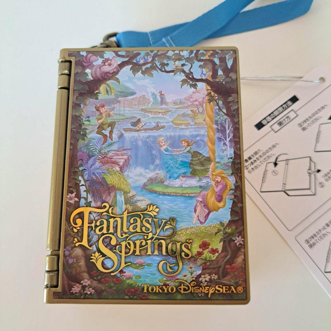 Front view of the Tokyo DisneySea Fantasy Springs book-shaped candy case showing its colorful illustrated cover and attached blue strap.