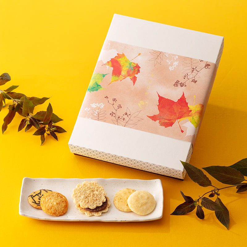 A decorative box of packaged rice crackers shown with a plate of assorted rice crackers on a yellow background.