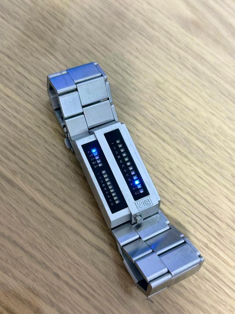 Tokyoflash Twelve 5-9 LED stainless steel wristwatch with two vertical LED displays lit, photographed on a wooden surface.