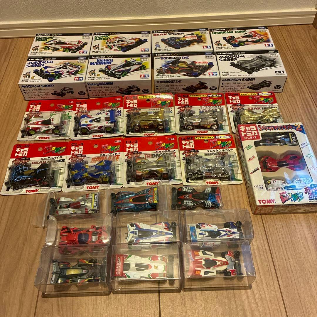 Multiple Tomica Let’s & Go character metal toy cars in boxes and blister packs arranged on a wooden floor.