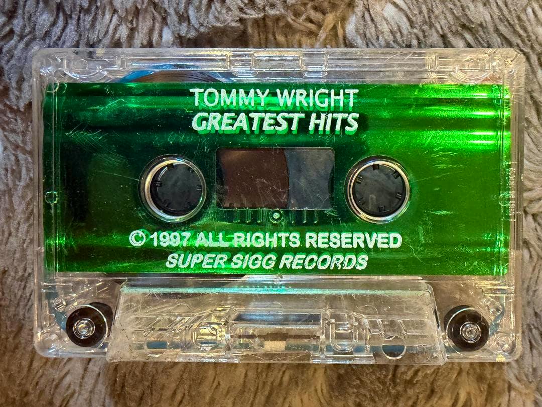 Top-down view of a clear cassette tape in its case with a green label reading “TOMMY WRIGHT GREATEST HITS.”