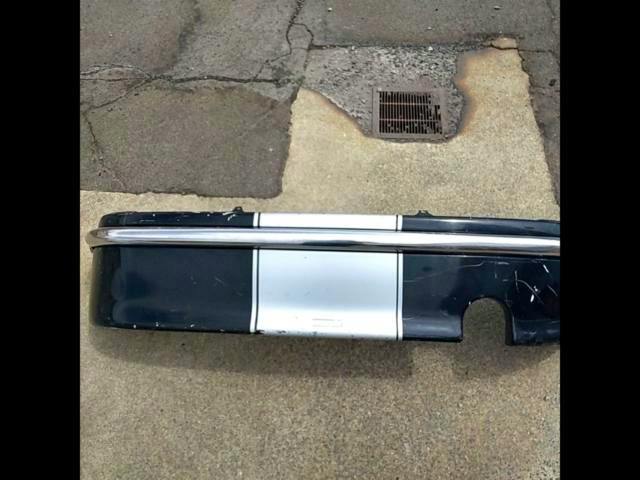 March/HK11 Tommykaira M13 Stage II rear bumper lying on pavement, black with a central silver section and chrome trim.
