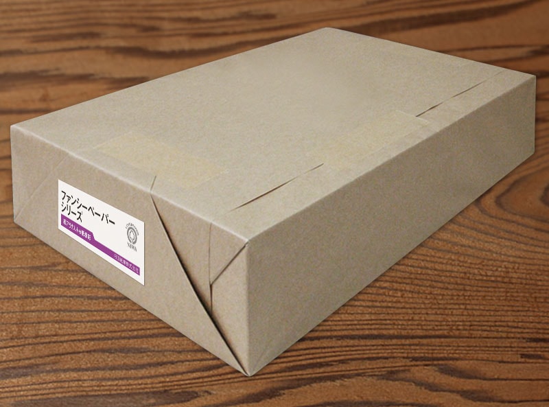A kraft-wrapped ream of printer paper on a wooden surface with a small label on one end.