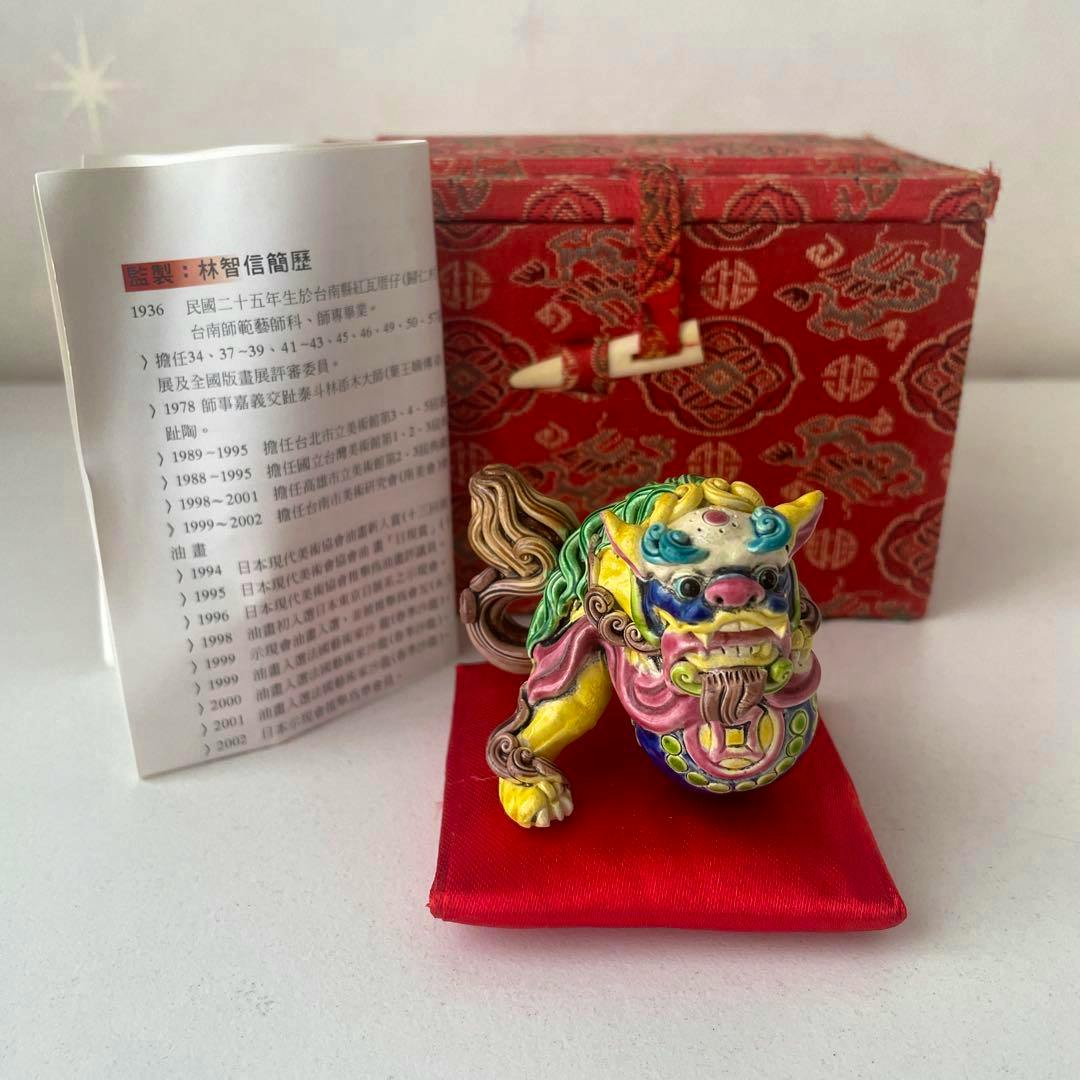 Colorful ceramic Tang lion figure displayed on a red cushion with a red patterned box and an instruction booklet behind it.
