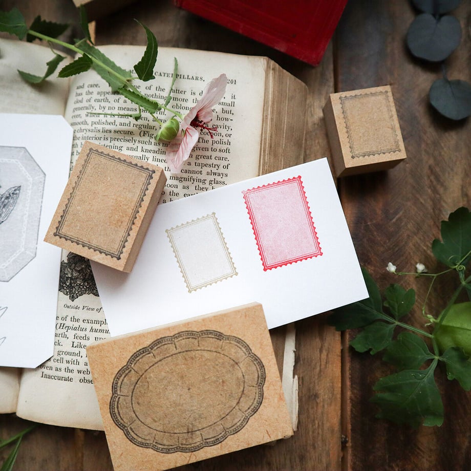 Three wooden stamp blocks with postage-style stamp impressions on paper, shown on an open book and wooden surface.