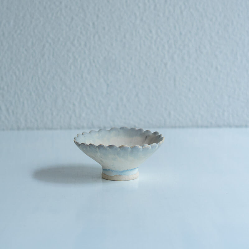 A small ceramic flower-shaped plate with scalloped edges on a short pedestal, shown on a white surface.