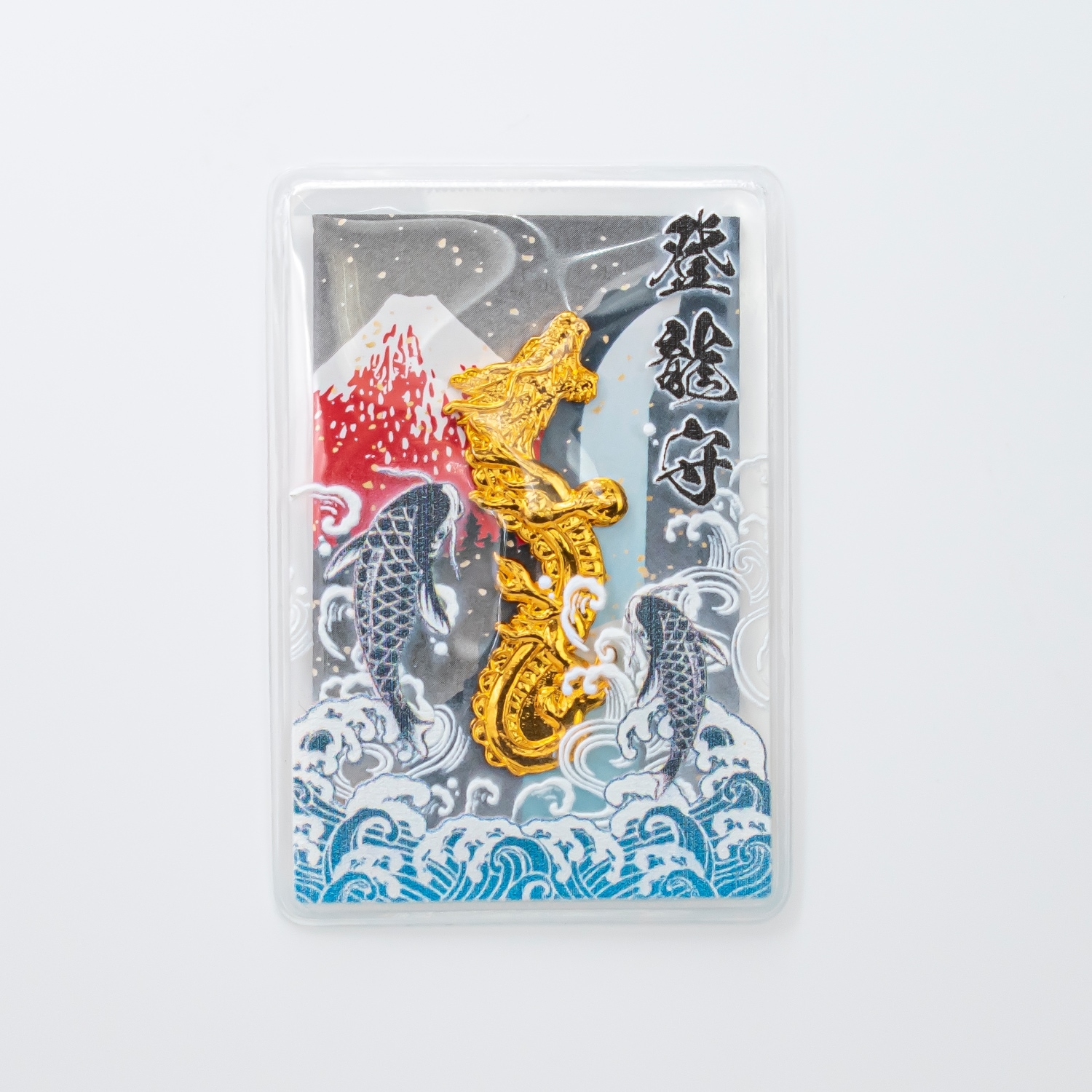 A gold dragon-shaped amulet (登龍守) displayed in a clear plastic case with decorative waves, koi, and Mount Fuji in the background.