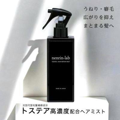 Black rectangular spray bottle of トスヴェールヘアリペアミスト (hair repair mist) on a white pedestal with Japanese text in the background.