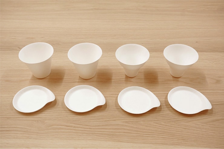 Four white paper sample cups with matching small saucers arranged on a wood surface.