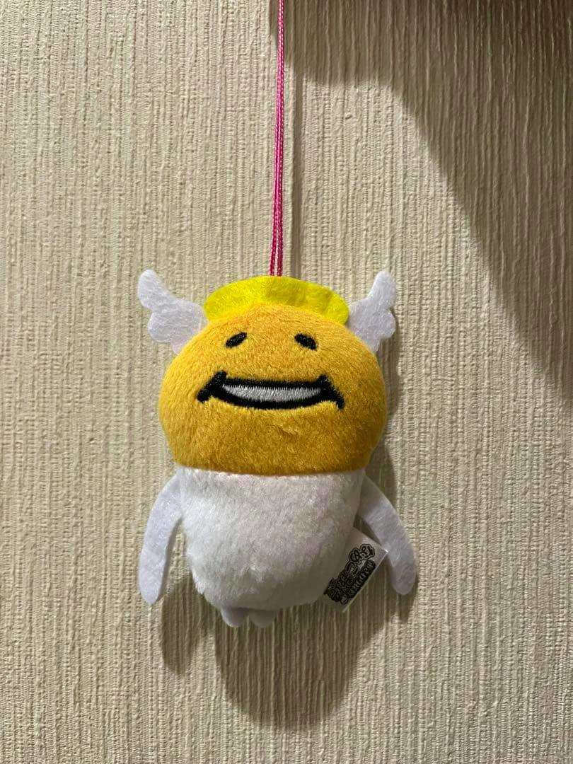 Angel-themed Nameko plush mascot cleaner hanging from a pink cord against a textured wall.