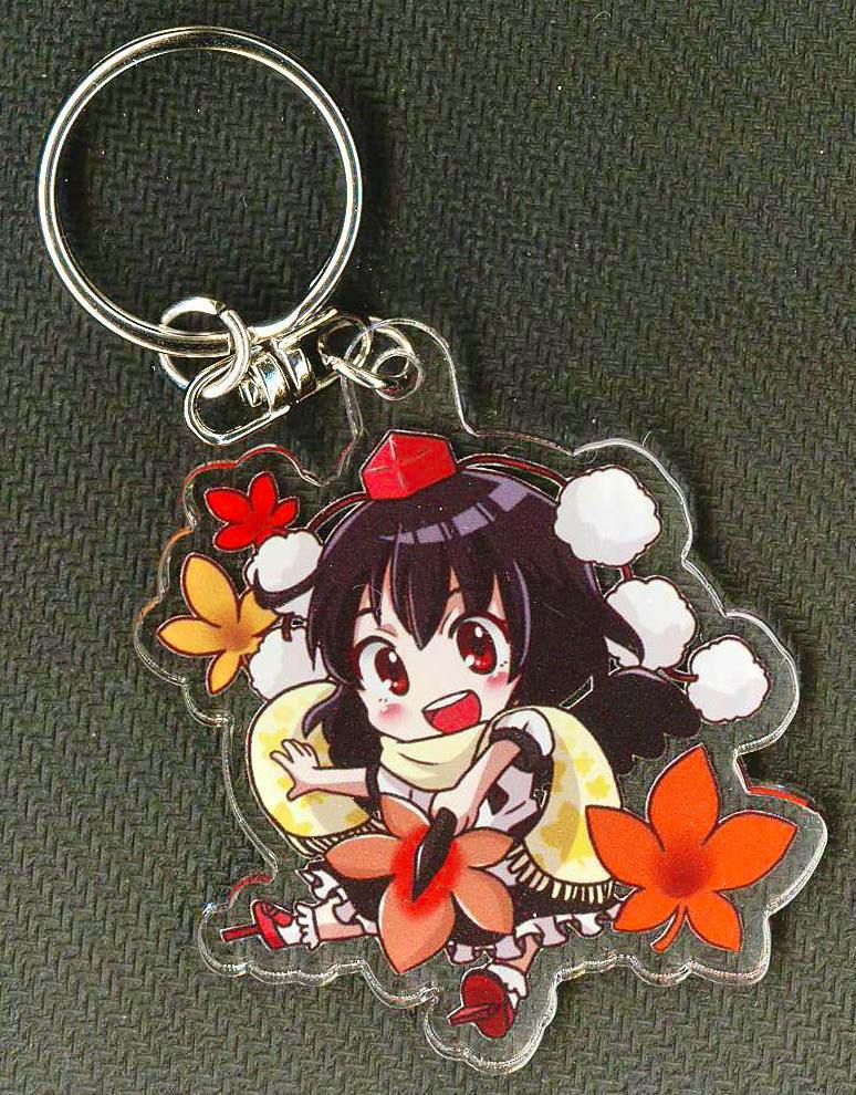 An acrylic keychain of Aya Shameimaru (Touhou Project) shown on a dark green textured background.