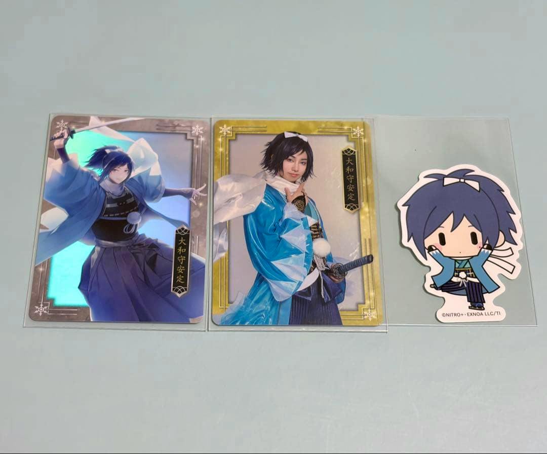 Flat photo of three items: a holographic photocard, a portrait photocard of 大和守安定 (Yamato no Kami Yasusada), and a chibi character sticker.