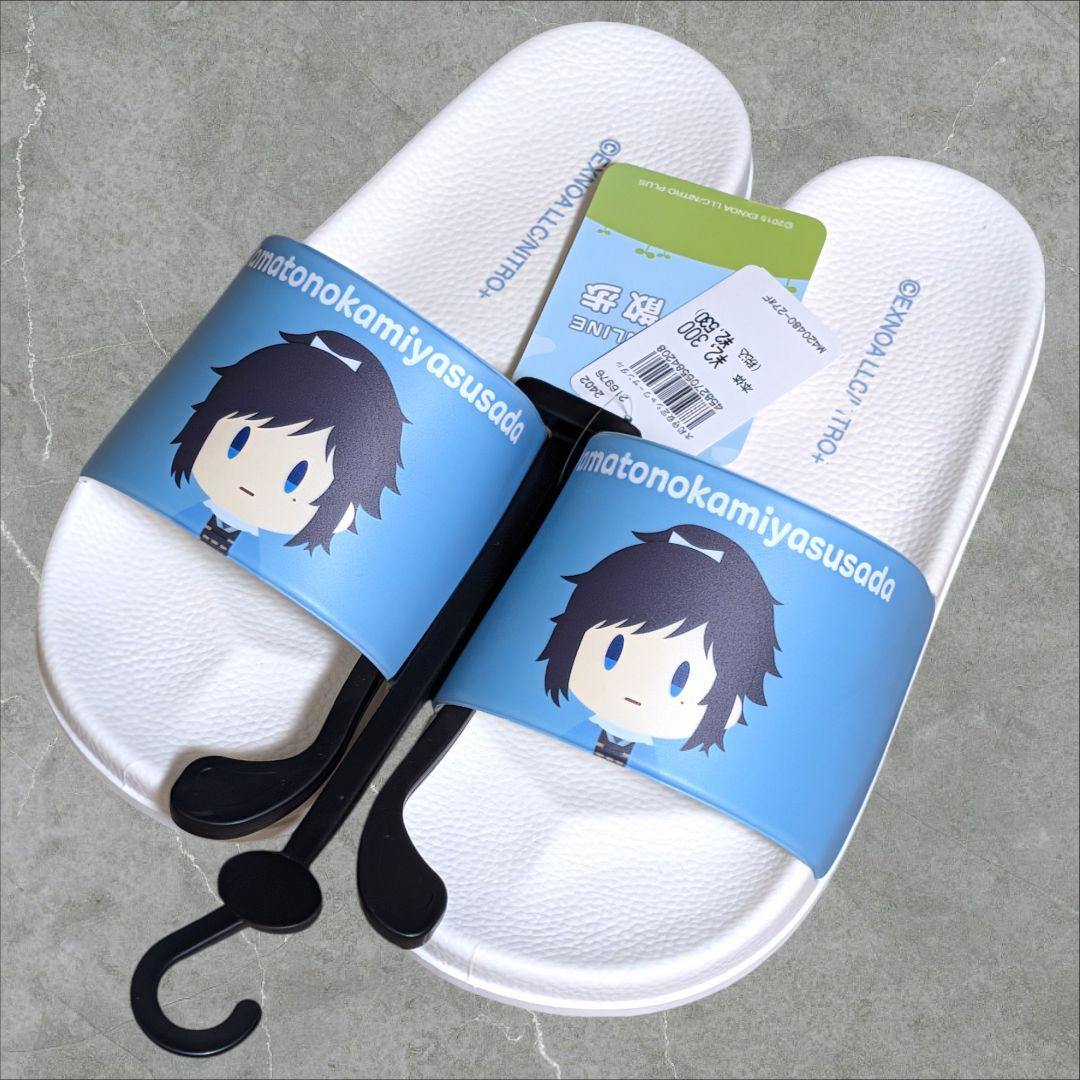 Pair of white shower slippers with blue straps printed with a chibi character from Touken Ranbu and attached retail tags, photographed on a gray surface.