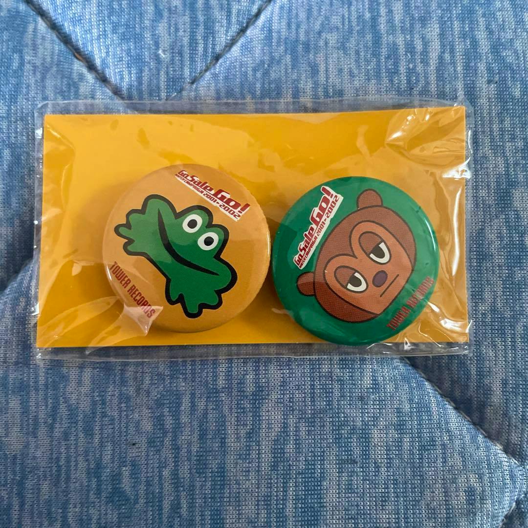 Two round pin badges sealed on a yellow card, one with a green frog design and one with a brown bear design.