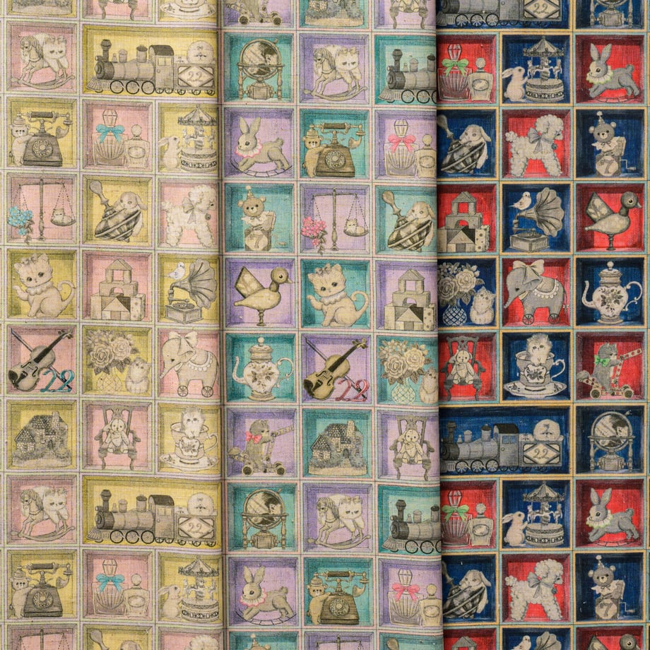 Photo of the TOYナイトボックス cotton-linen sheeting fabric showing a repeating toy-in-box motif in multiple color panels.