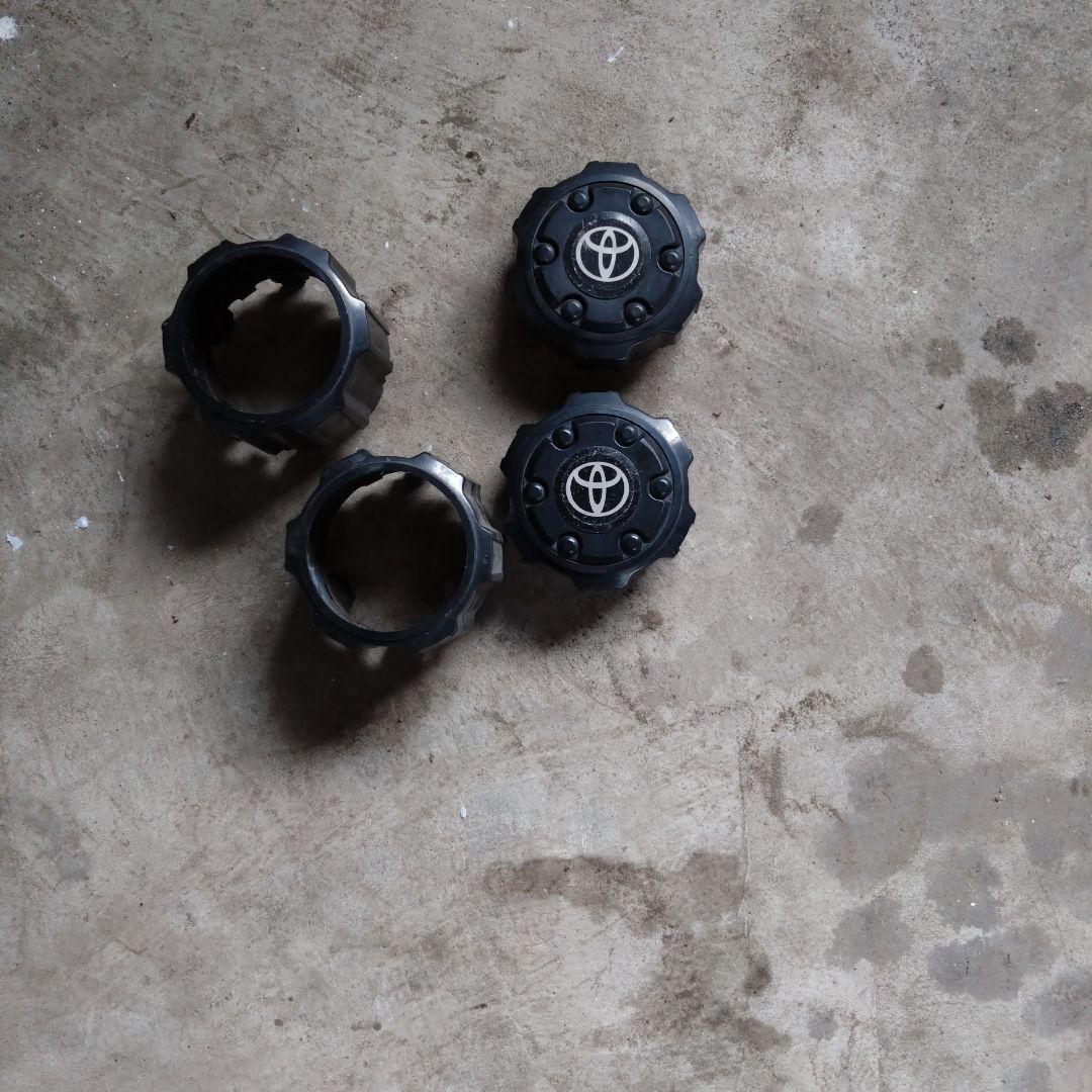 Four Toyota Land Cruiser Prado 78w wheel caps, two showing the Toyota logo, laid on a concrete floor.