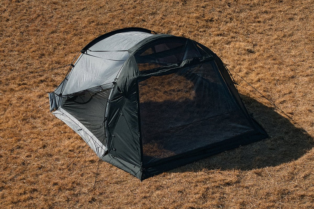 A dark-colored tent with a large front TPU window pitched on dry grass.