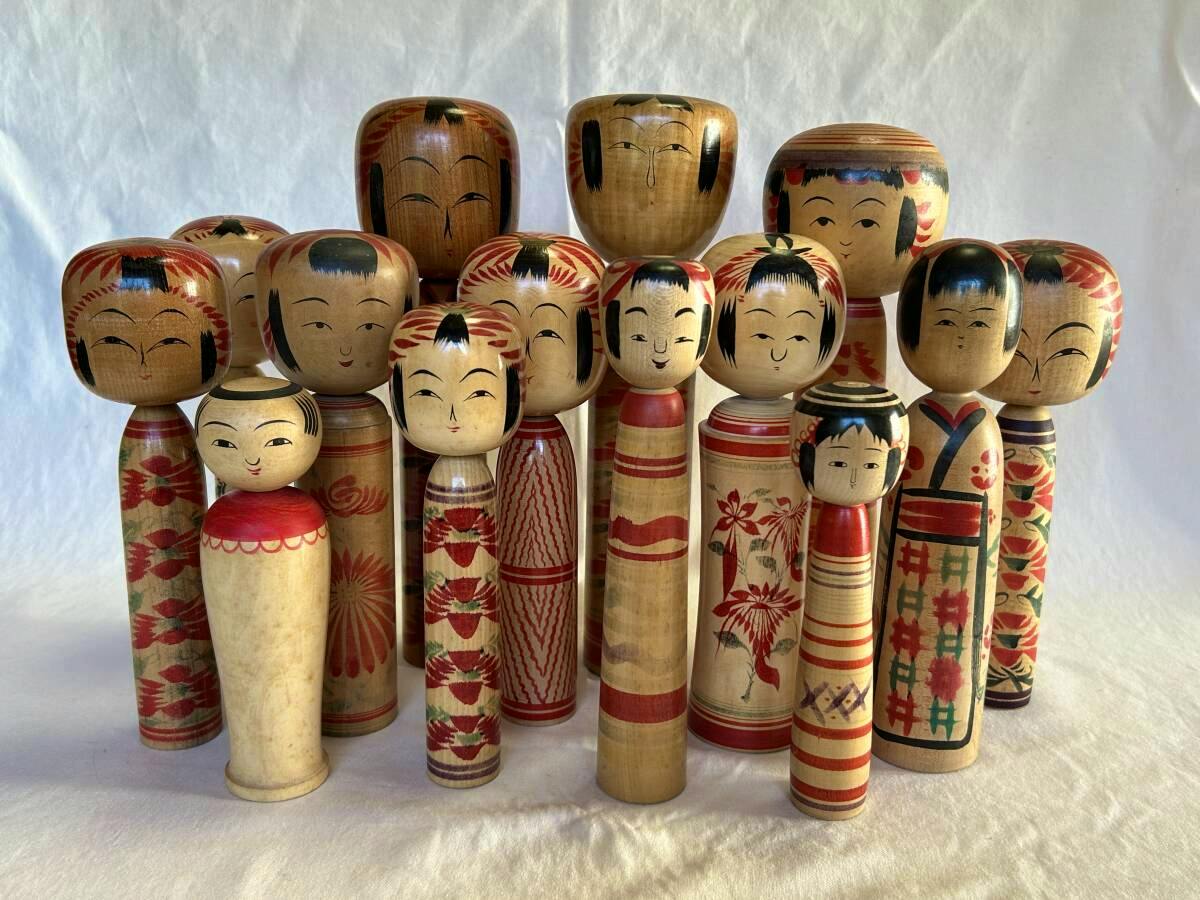 Fourteen traditional wooden kokeshi dolls of varying heights arranged standing on a white cloth background.
