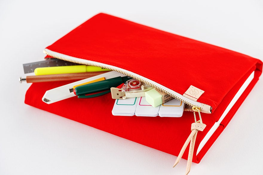 Red A5 cousin-size polyester book cover with a zippered pouch partially open revealing pens and small items.