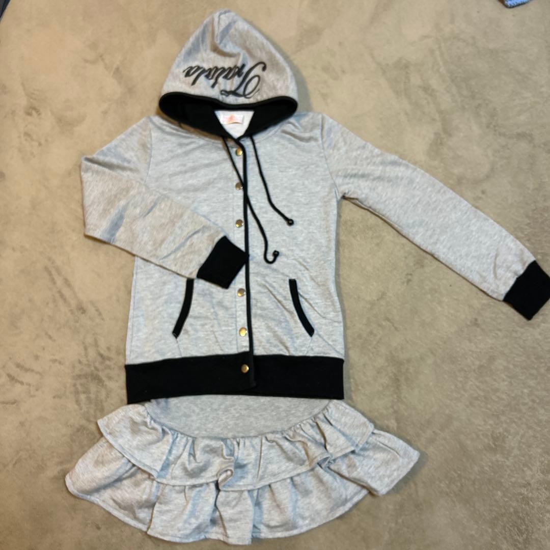 Gray Tralala hooded jacket with black trim and a matching ruffled skirt laid flat on a beige surface.