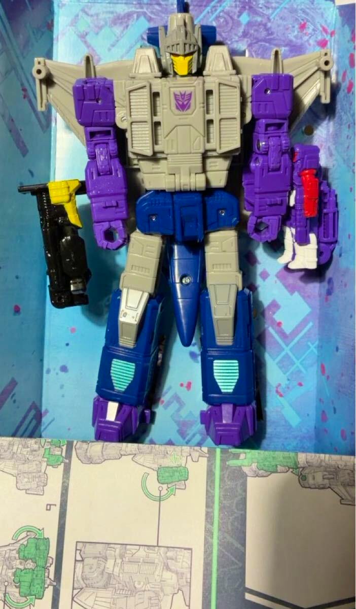 Front view of the Transformers Legacy Evolution Needlenose plastic figure in robot mode laid in its packaging tray with accessories.