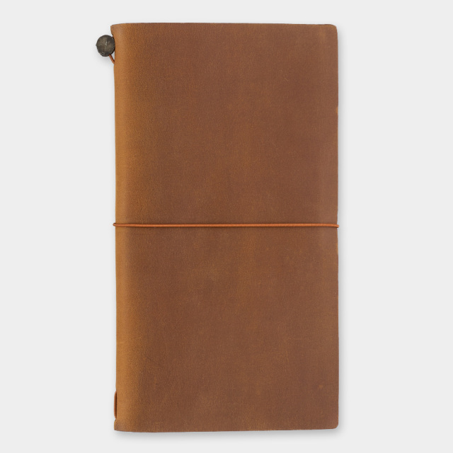 A closed camel-colored cow leather traveler's notebook cover secured with an elastic band.