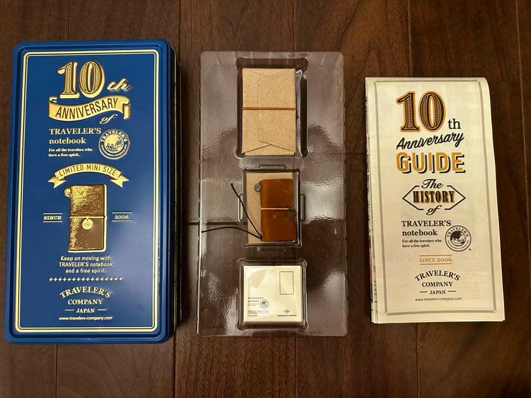 10th Anniversary Traveler's Notebook mini tin set showing the blue tin, the camel mini notebook in a plastic tray, and the guide booklet.