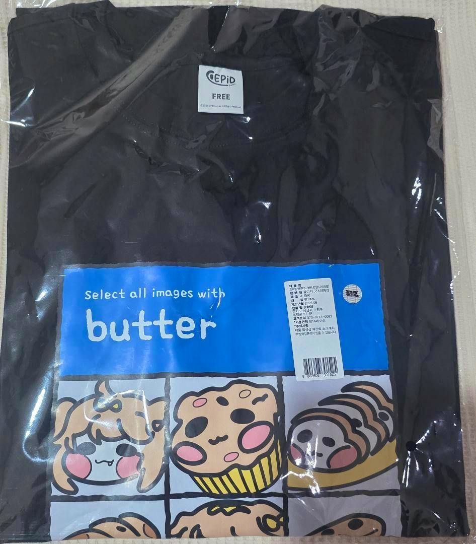 Folded black T-shirt in plastic packaging showing a blue panel with the word "butter" and cartoon pastry graphics, plus a visible "FREE" neck tag.