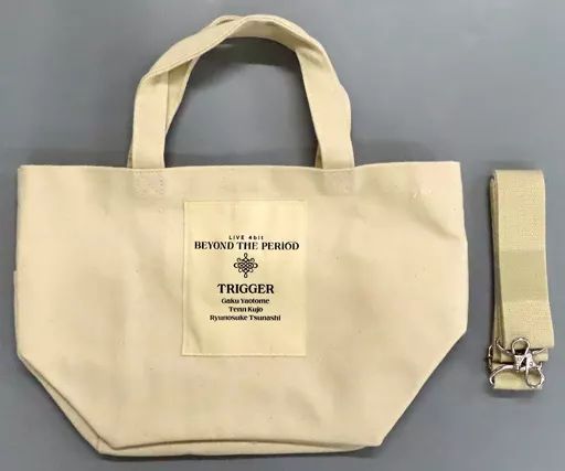 Beige mini tote bag with a printed patch reading "BEYOND THE PERIOD TRIGGER" shown next to a beige strap with metal clips.