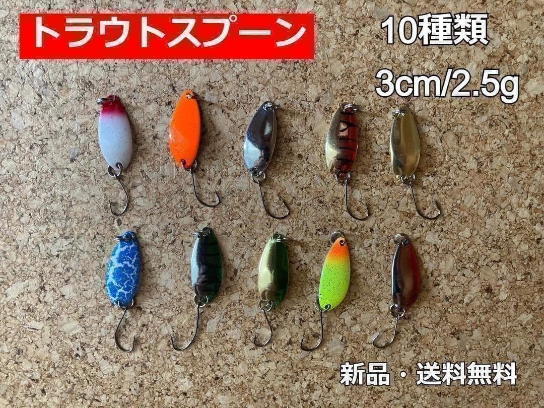 Ten small metal trout spoon fishing lures in various colors arranged on a cork surface.