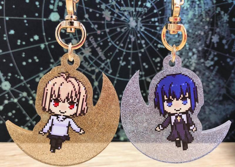 Photo of two moon-shaped glitter acrylic keychains with pixel-art characters, one gold with a light-haired character and one silver with a blue-haired character, attached to gold clasps.