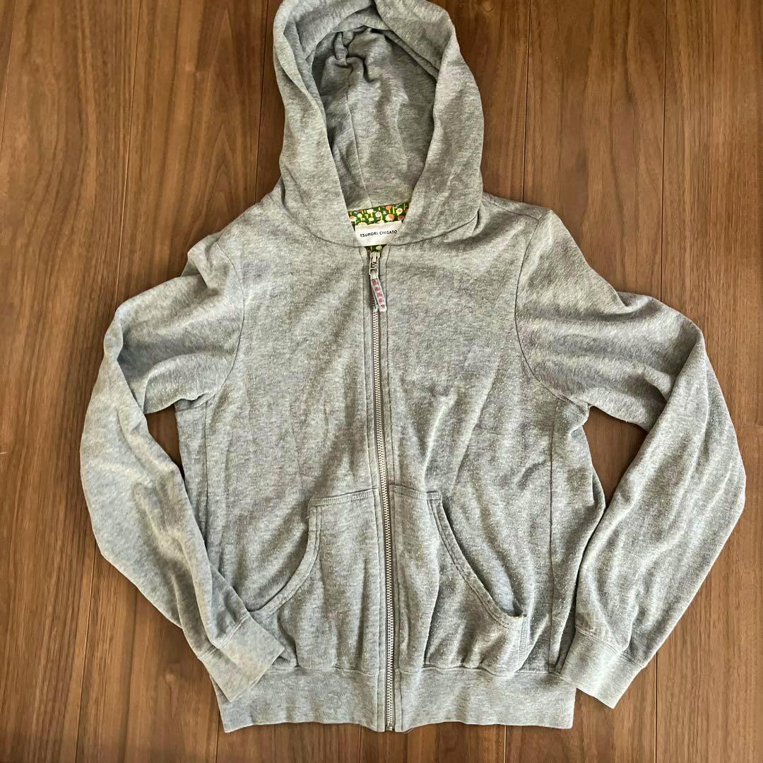 Gray cotton zip-up sweatshirt (hoodie) laid flat on a wooden floor, showing the front zipper, hood, kangaroo pockets, and sleeves.